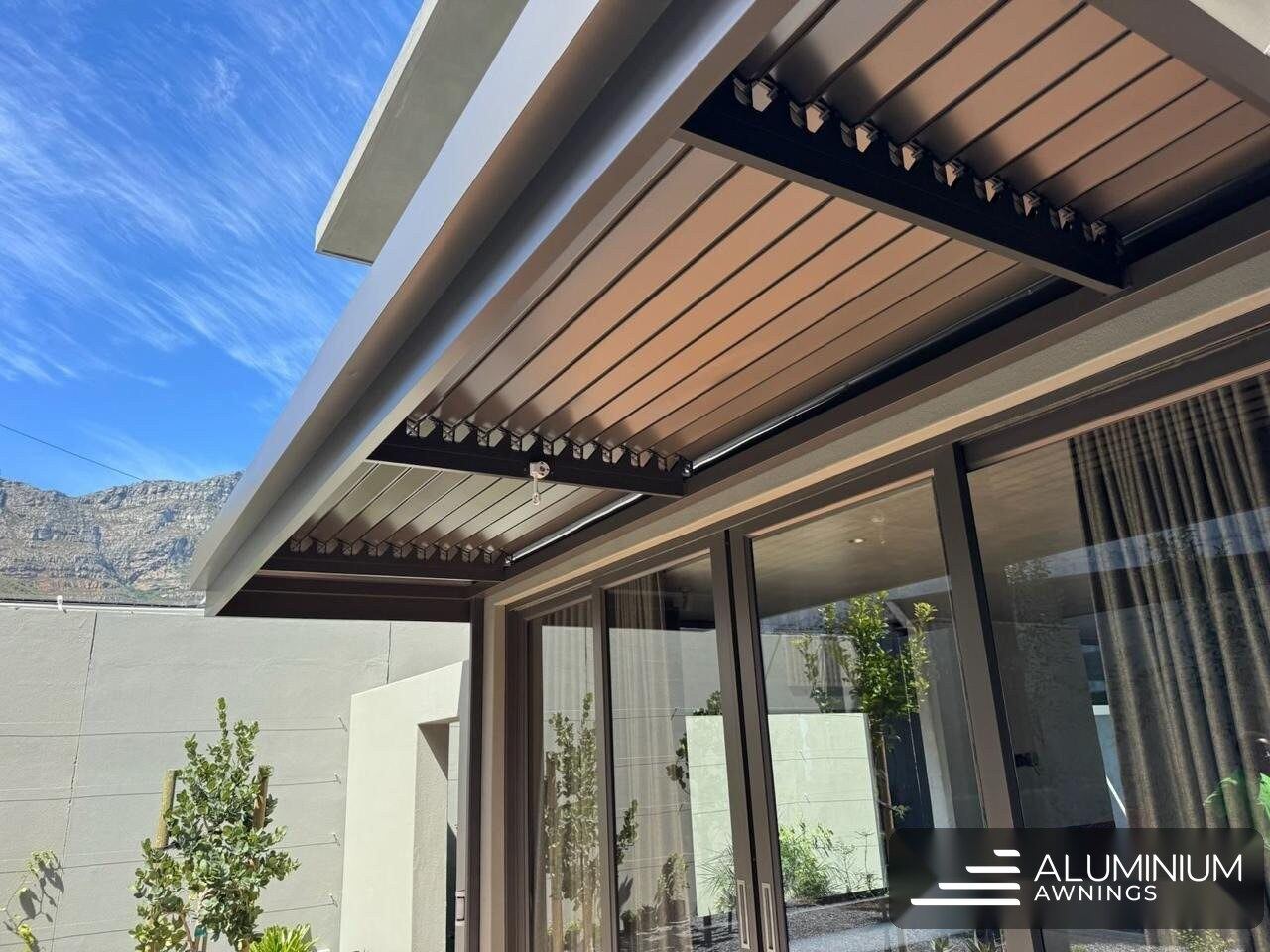 Umber grey motorised louvre roof spanning a clifftop patio with direct Atlantic Ocean views — Bakoven, Cape Town
