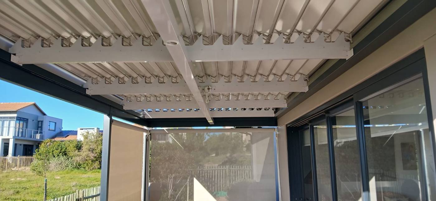 White louvre blades seen from below, with two drop blinds part-lowered on the sides of the patio