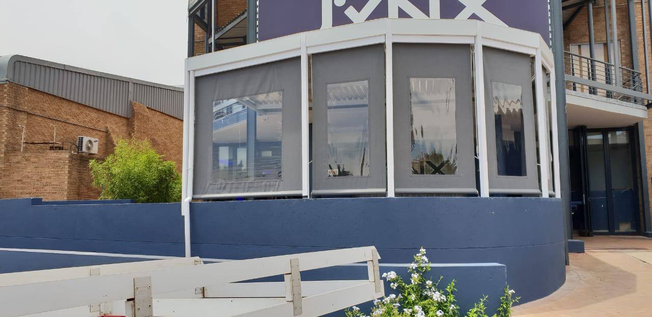 Grey drop blinds with clear PVC windows enclosing a curved venue terrace