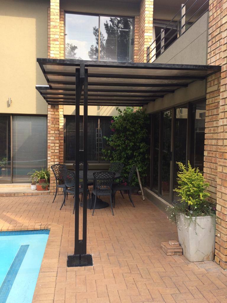 Clear polycarbonate awning on a black frame over a poolside entrance walkway