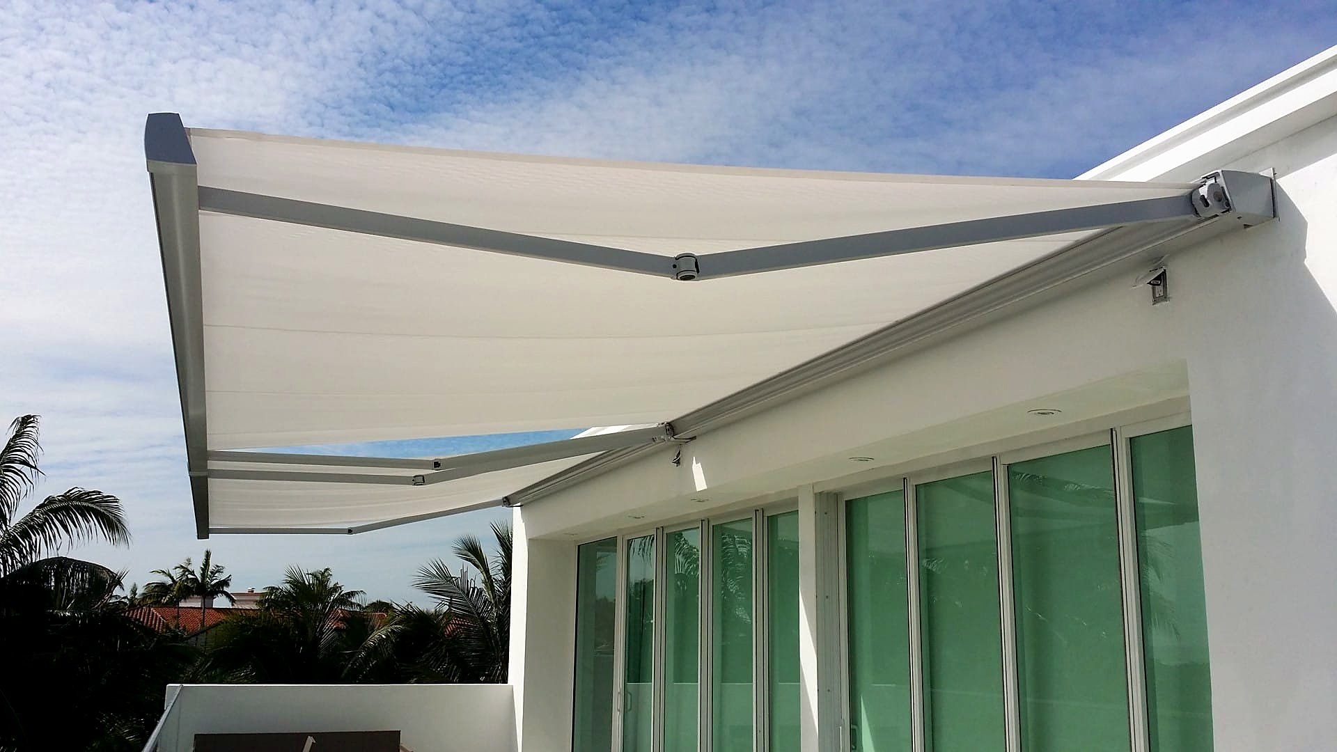 Cream folding-arm retractable awning wound out over the glass doors of a white modern house