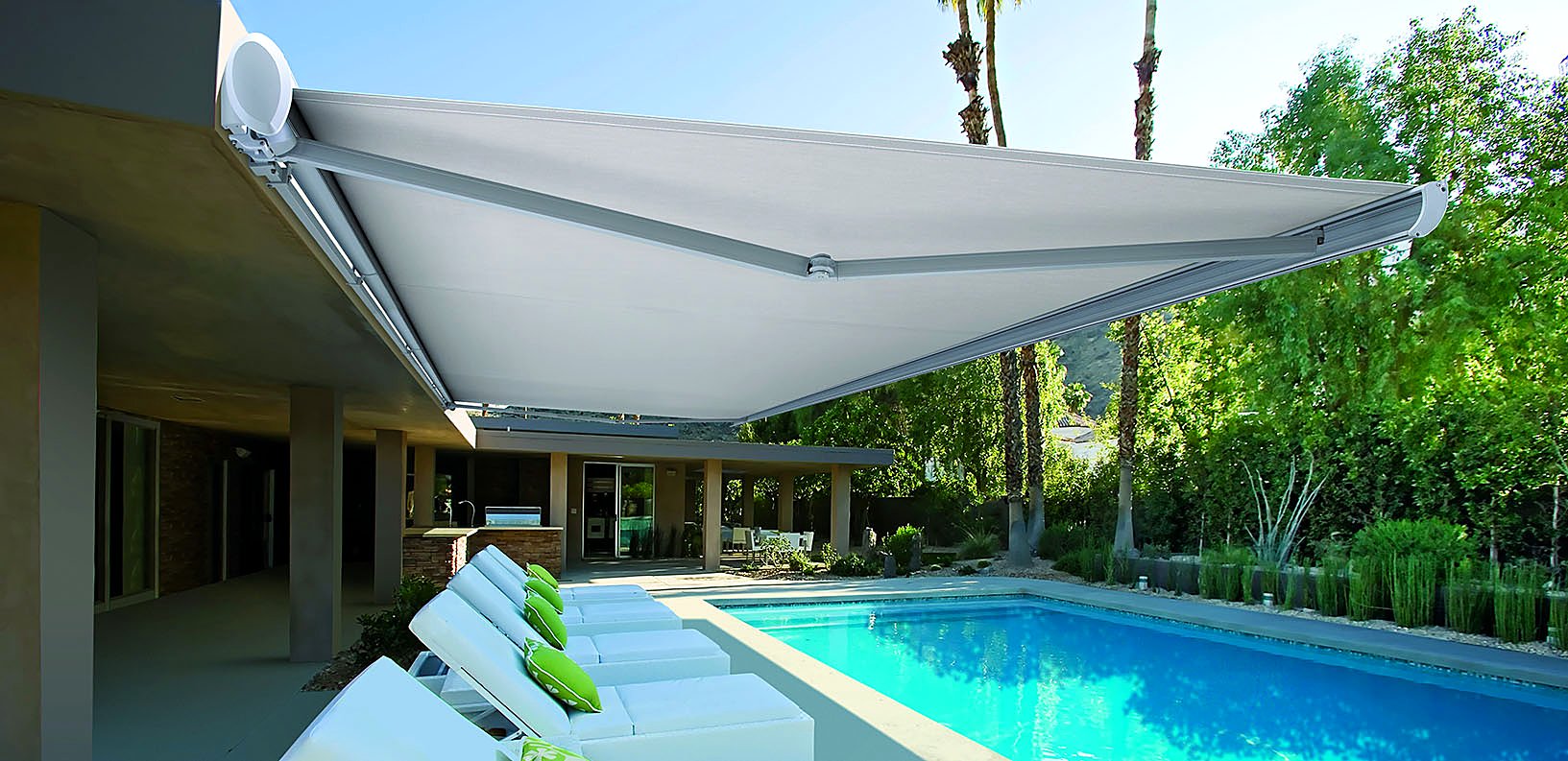 White full-cassette retractable awning wound out over a pool terrace with sun loungers
