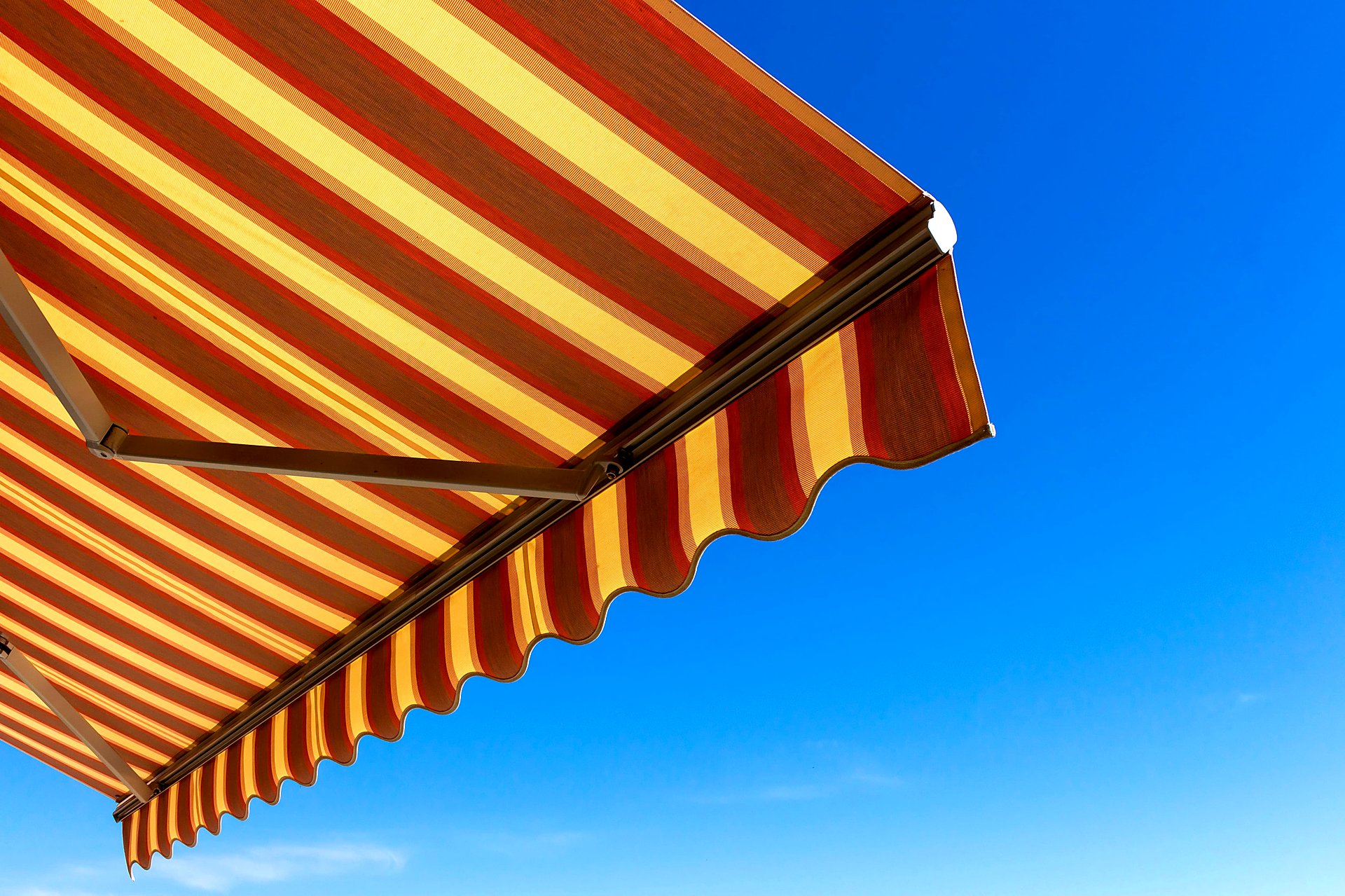 Underside of a red and yellow striped retractable awning with a scalloped valance